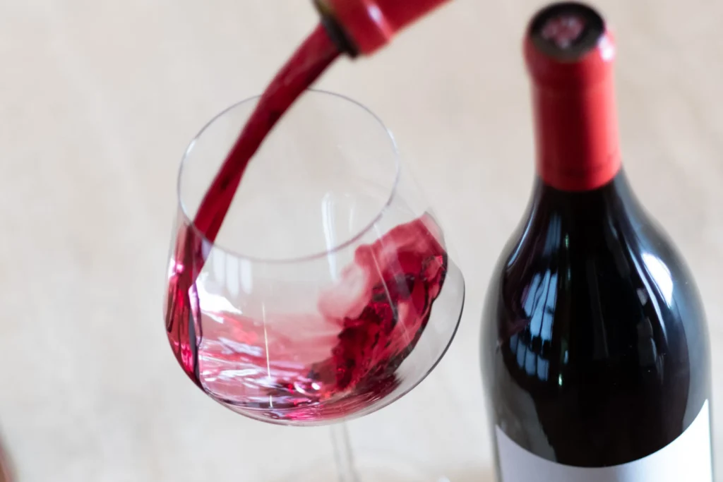 A la izquierda, hay una copa en la que se está sirviendo vino tinto fino, que está situada junto a una botella. Esta imagen se utiliza para ilustrar una entrada sobre las diferencias entre el vino joven, el crianza, el reserva y el gran reserva.
